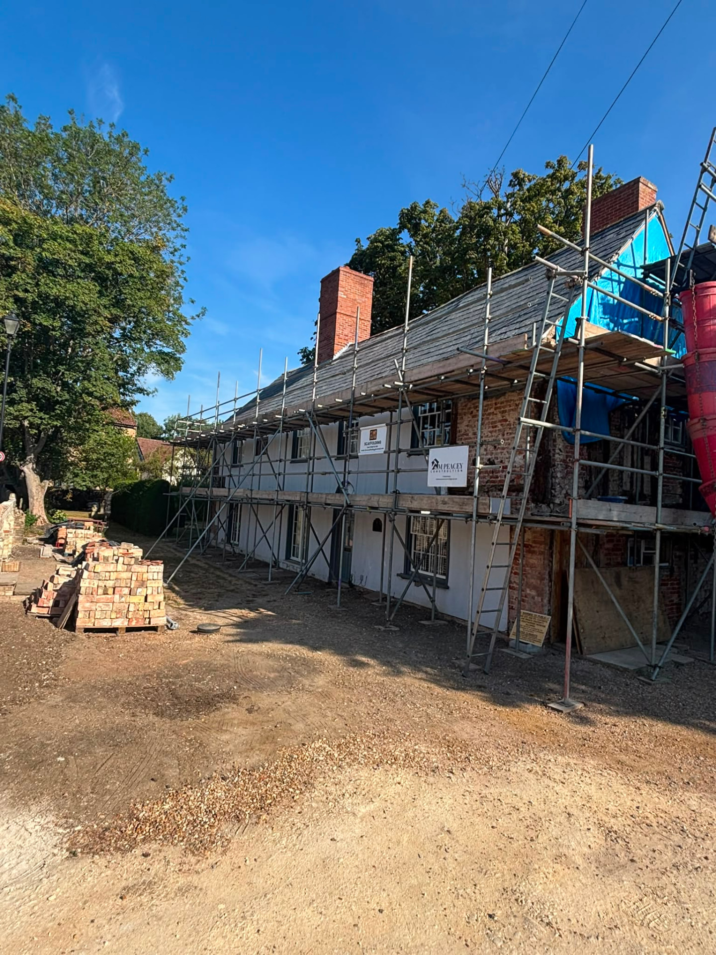 Large period building with Elms Scaffolding erected around the roof and elevation, blue weather protection sheeting and brick stacks on site